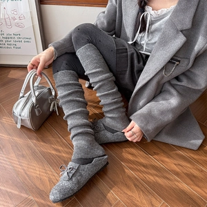 Detail of grey ribbed knit leg warmers paired with grey bow loafers on wood floor
