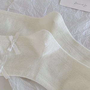 Dettaglio di calzini bianchi con pizzo, fiocchi di seta e trama a maglia fine