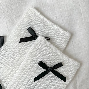 Detailed knit texture of white leg warmers with delicate black satin bow accents