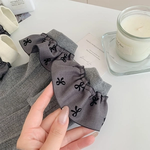 Detail von grauen Rippstrick-Socken mit Rüschenkante und schwarzer Schleifenstickerei