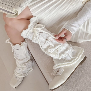 Detail of cream white pointelle knit leg warmers with drawstring ribbons and ruffled edges