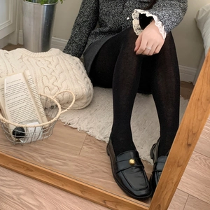 Mocassins noirs élégants à boucle dorée et collants noirs sur parquet en bois