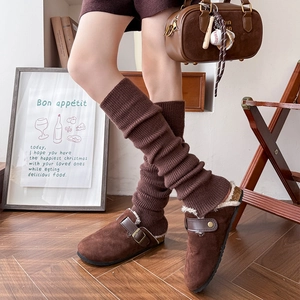 Brown knitted leg warmers paired with suede mules and metal buckles on wooden floor