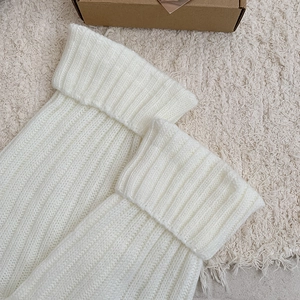 Close-up of white ribbed knit leg warmers with folded cuff detail on soft beige rug