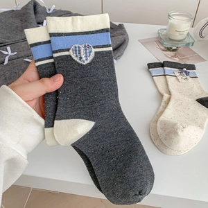 Detail of grey knit sock with pearl heart patch and blue plaid bow in cozy home setting