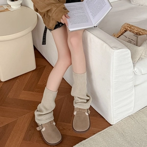 Close-up of beige knitted rib leg warmers paired with brown suede mule shoes
