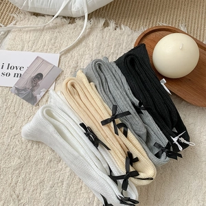 Close-up of knit calf socks with bow details in white, beige, grey and black colors