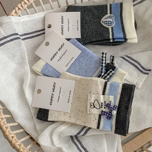 Detail of three pairs of knit socks featuring bows, pearls, and bear embroidery in a basket
