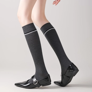 Detail of dark grey knee-high socks with white stripes and black Mary Jane shoes
