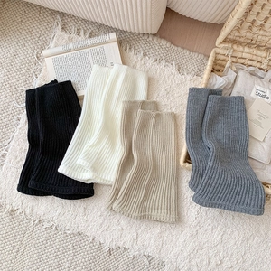 Flat lay of ribbed knit leg warmers in black, white, beige, and grey on a plush rug
