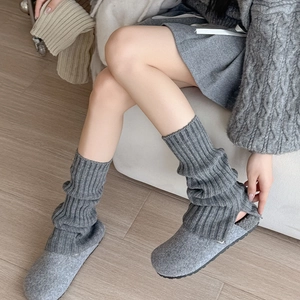 Detail of grey ribbed knit leg warmers paired with cozy felt mule slippers on wooden floor