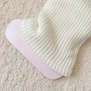 Detail of white rib-knit leg warmer with vertical textured pattern and soft wool texture
