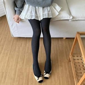 Close-up of dark grey ribbed tights paired with white skirt and black bow shoes
