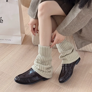 Detailed close-up of cream chunky knit leg warmers paired with dark brown loafers