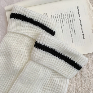 Detail of white knit leg warmer with black stripe showing coarse texture on soft background