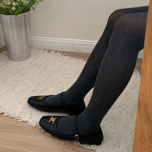 Détail de collants gris foncé portés avec des chaussures Mary Jane noires à boucle d'or