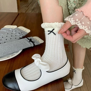Detailed macro view of white cotton mid-tube socks with elegant black bow and lace trim