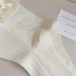 Detailaufnahme der cremefarbenen Rippsocken mit eleganter Spitze und Schleife