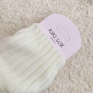 Macro detail of cream vertical ribbed knit leg warmers with branded packaging tag