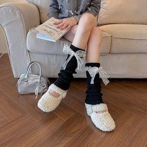 Détail de jambières en maille noire avec nœuds en dentelle blanche et chaussures en molleton