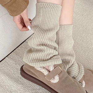 Close-up of beige knitted leg warmers featuring thick vertical textures and soft folds