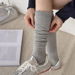 Detail of grey knitted stirrup leg warmers with ruffle cuffs and silver sneakers