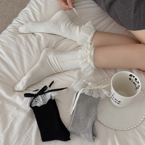Detail of soft knit socks featuring delicate lace trim and ribbon bows in black and white