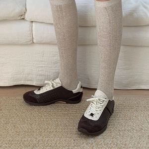 Detail of beige ribbed knee-high socks worn with brown and white retro sneakers