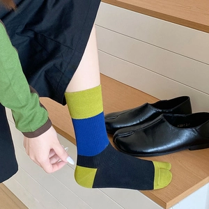Detail of color-block Tabi split-toe socks in green and blue worn with black leather shoes