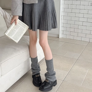 Detail of grey ribbed knit leg warmers paired with black loafers and a mini skirt