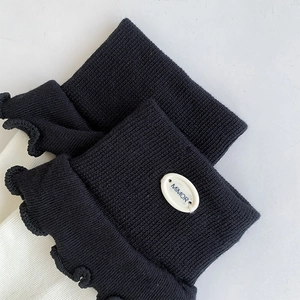 Close-up of black knitted socks featuring elegant ruffle trim and branded white button