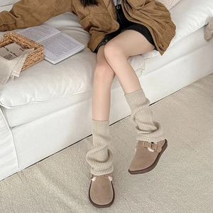 Close-up of cream chunky knit leg warmers paired with brown suede sheepskin mules