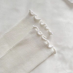 Close-up of white ribbed knit fabric featuring delicate ruffle trim edges in balletcore style