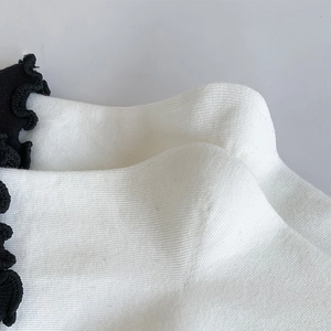 Close-up of white knitted socks with black ruffled trim and detailed texture finish