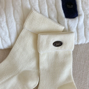 Close-up of ribbed off-white mid-calf socks with decorative bow emblem detail