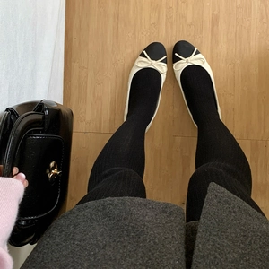 Detail of black vertical ribbed tights paired with bicolor bow ballet flats on wood floor