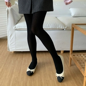 Women's slim black vertical striped tights paired with stylish ballet flats indoors