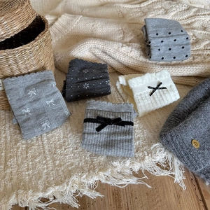 Detailed close-up of various grey knit leg warmers with bows on a cozy beige blanket