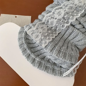 Détail de jambières en tricot gris avec bordure en dentelle blanche sur bois