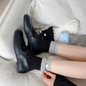 Detail of ruffled cuff socks paired with black Mary Jane flats on a soft sofa