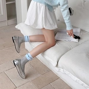 Detail of grey knit crew socks with blue ruffled edges paired with silver ballet flats