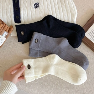 Close-up of ribbed knit crew socks featuring elegant decorative buttons and gold accents