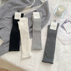 Detailed close-up of knit leg warmers in black, white, and grey with ruffle trim edges
