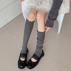 Detail of grey knitted leg warmers with vertical ribs and ruffled edges in ballet style