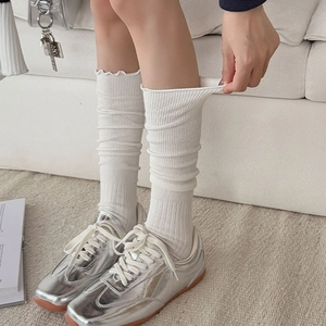 Close-up of white ribbed leg warmers with ruffle trim paired with silver ballet sneakers