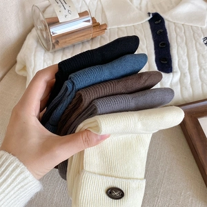 Detail of knitted mid-calf socks with ribbed texture and vintage metal button accent