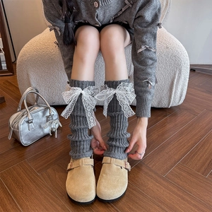 Detailed view of grey knitted leg warmers with delicate white lace ribbon bows