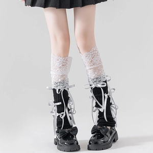 Close-up of black knit leg warmers with white lace trim and silver satin bows