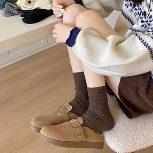 Detail of coffee brown knit socks with bow embroidery paired with warm suede clogs