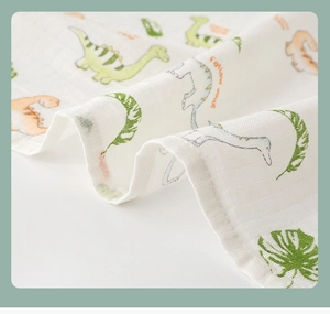 Close-up of soft cotton muslin baby swaddle with cartoon dinosaur and tropical leaf print
